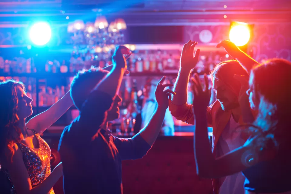 Dark shot of people dancing in front of bar with red and blue atmospheric lights